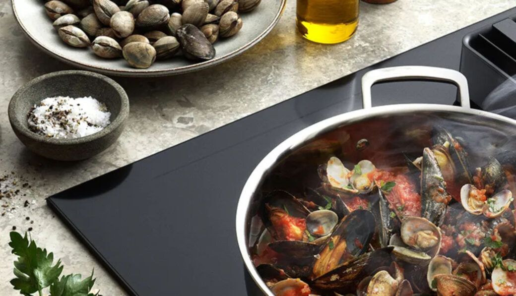 Pentola con spaghetti alle vongole su un piano a induzione nero